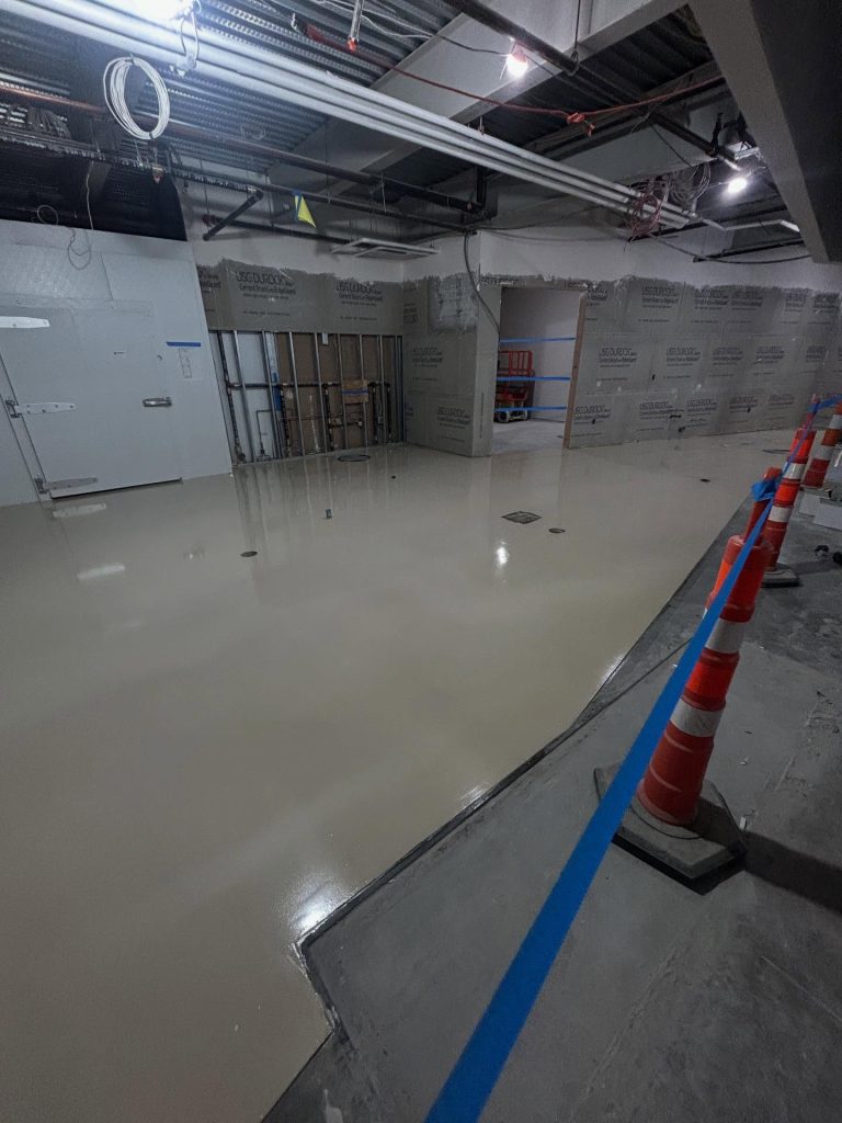 Commercial epoxy install in progress, wet white basecoat with traffic cones and cinderblock walls