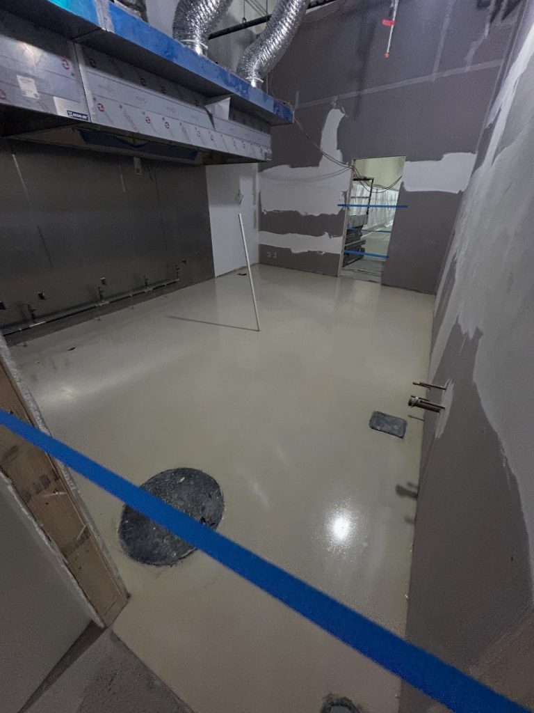 Commercial epoxy install in progress, white basecoat, overhead HVAC vents and blue tape