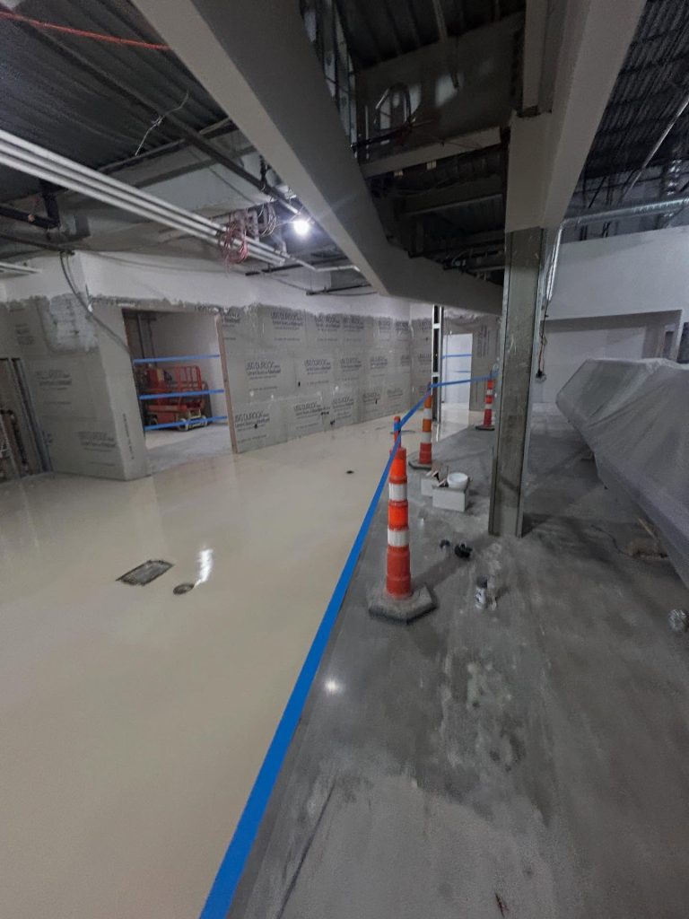 Commercial epoxy install in progress, wide interior view with traffic cones and drain covers