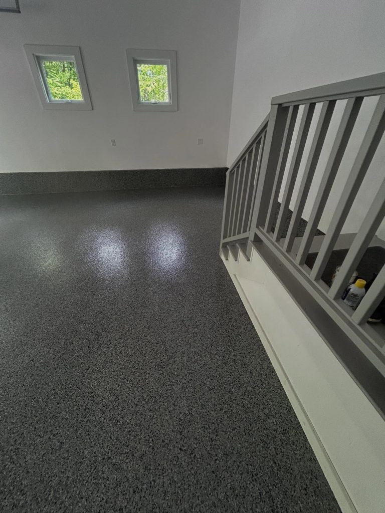 Dark grey flaked epoxy floor, finished basement with stair railing and windows