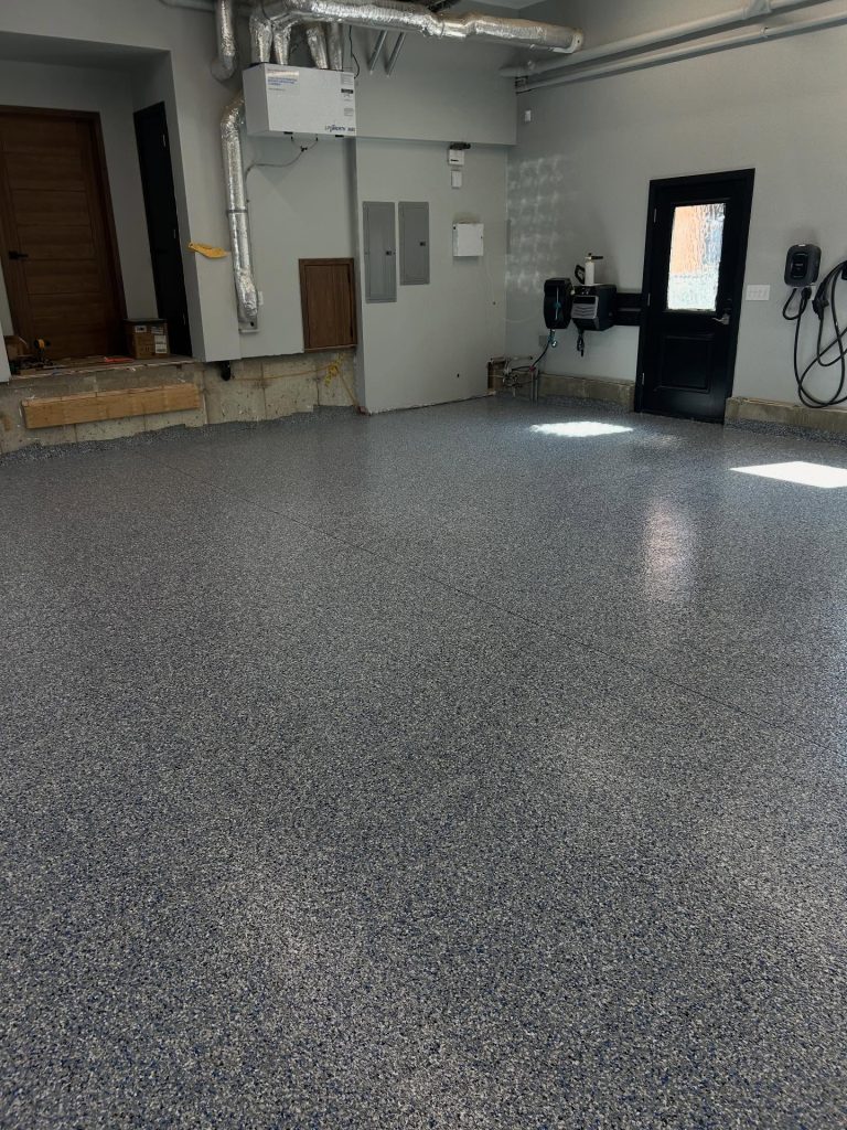 Grey flaked epoxy garage floor with baseboard trim and utility panel
