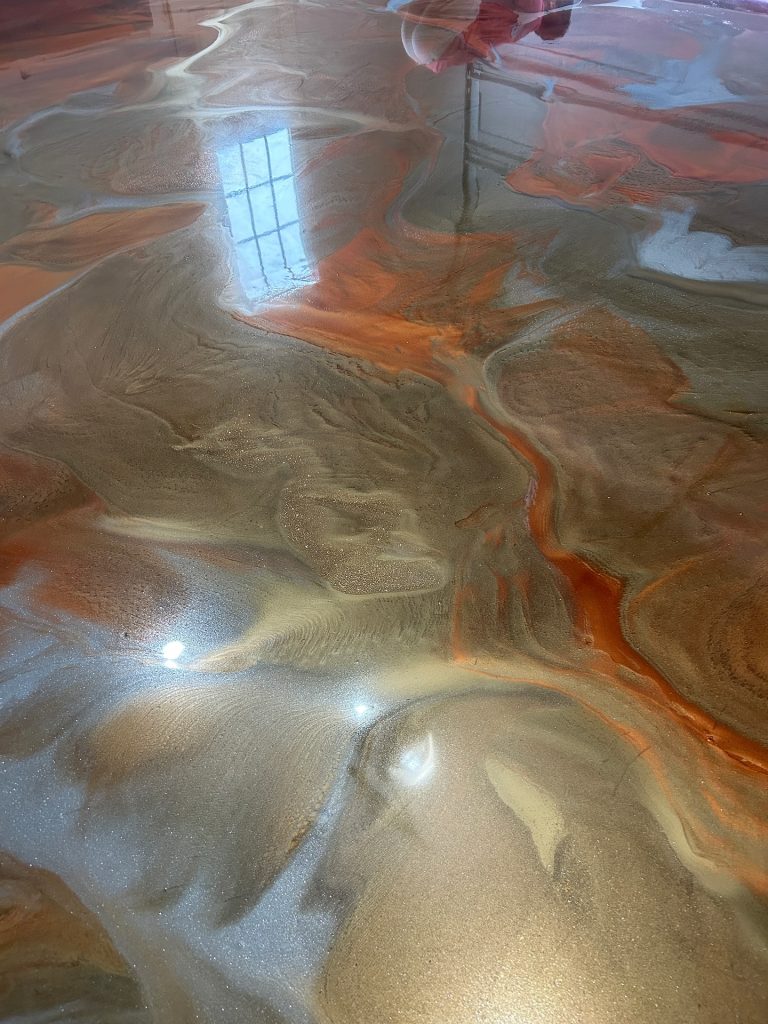 Metallic epoxy floor with copper, silver, and orange swirl, wide view with window reflection