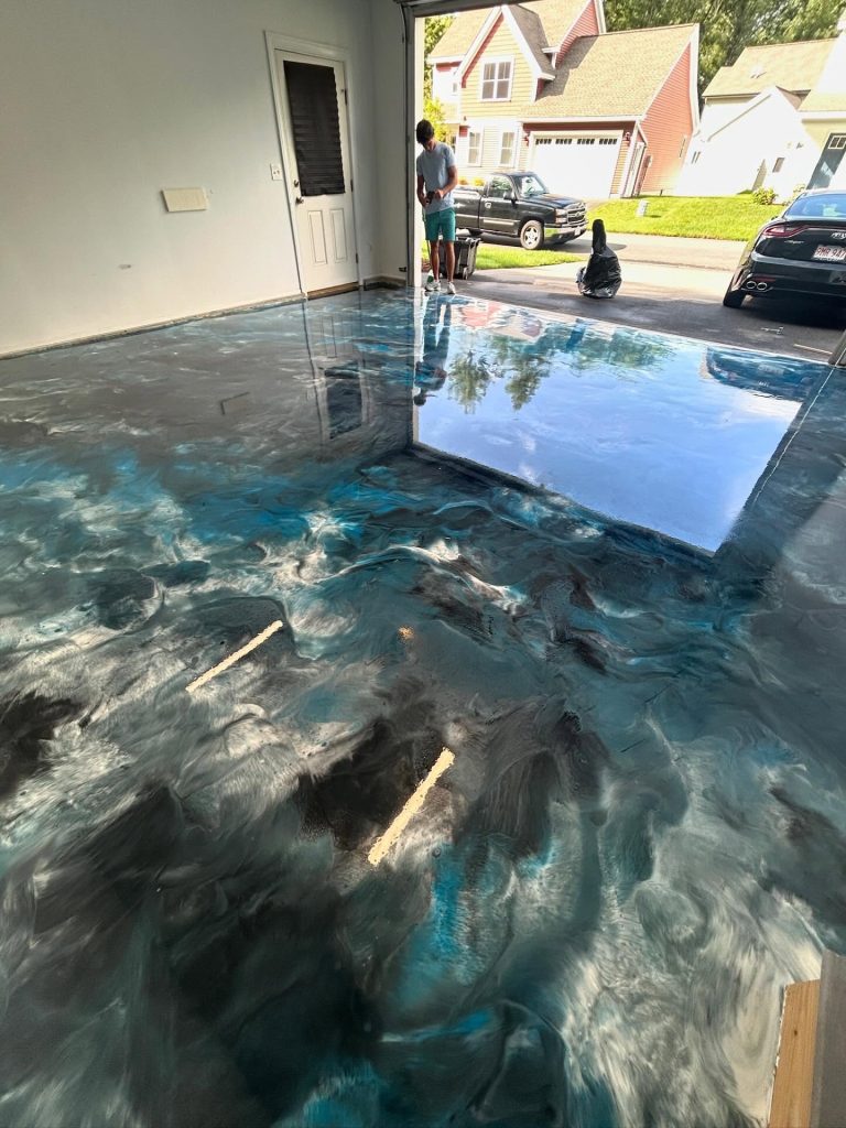 Blue and silver metallic epoxy garage floor with garage door open to a suburban driveway