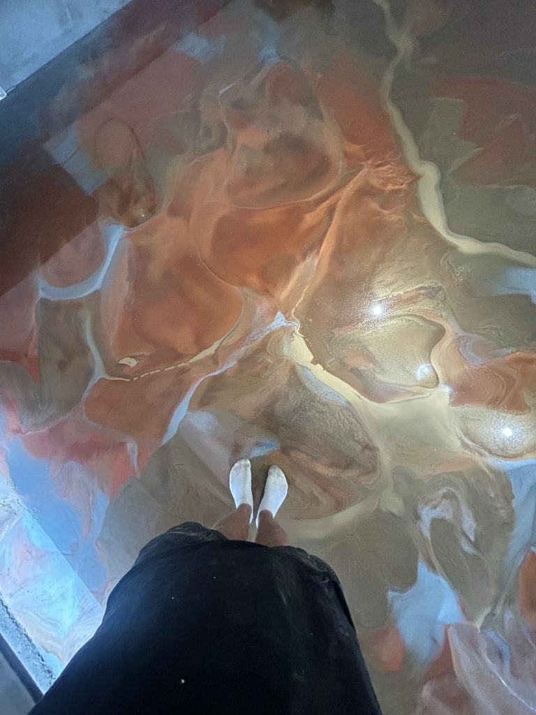 Metallic epoxy floor with orange and tan swirl, installer feet in frame