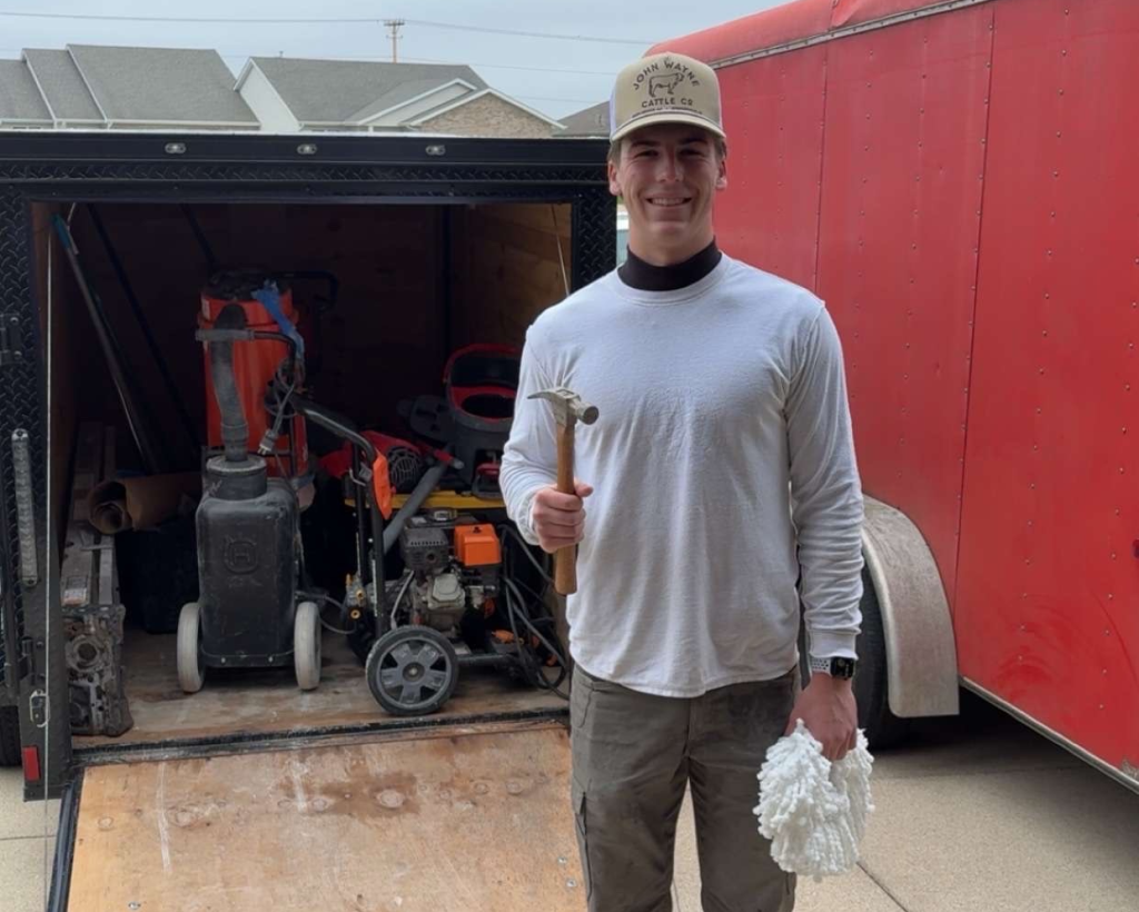 Trystin, owner of TD Epoxy Flooring, standing in front of his work trailer with concrete grinder and tools visible